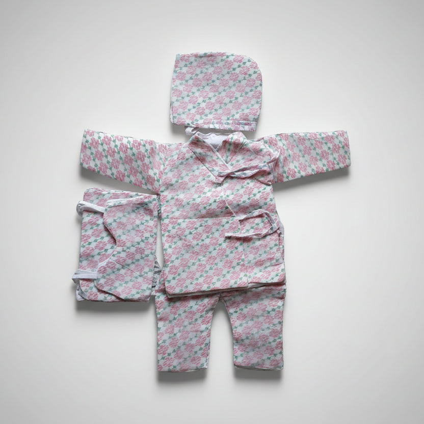 Traditional Nepali clothing set laid out on a surface, consisting of a pink and white checkered daura surwal, voto, and shoes for a newborn baby.