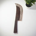 A handmade butcher's knife with a curved blade and a wooden handle, placed against a white background with a small potted plant to the side.