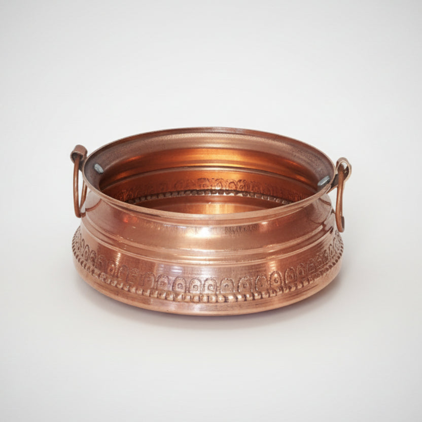 A copper khadkulo with embossed patterns and two handles.