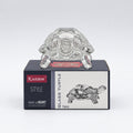 Glass turtle figurine with packaging on a white surface, blurred bookshelf in the background