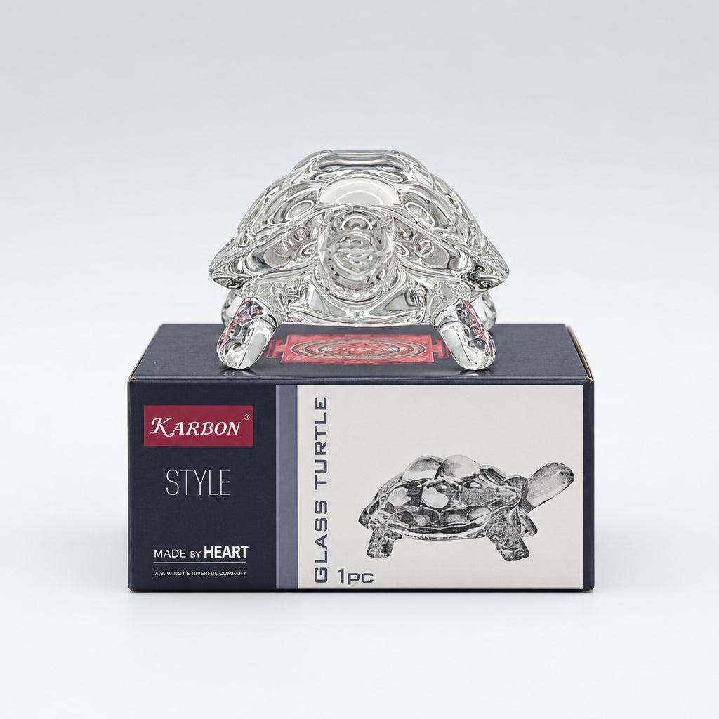 Glass turtle figurine with packaging on a white surface, blurred bookshelf in the background