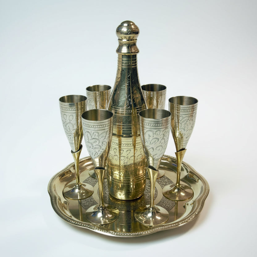 A set of metal stemware with a decorative pattern, including a decanter and glasses, displayed on a round tray.