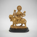 Gold figurine on a black base against a white wall with blurred shelves in the background