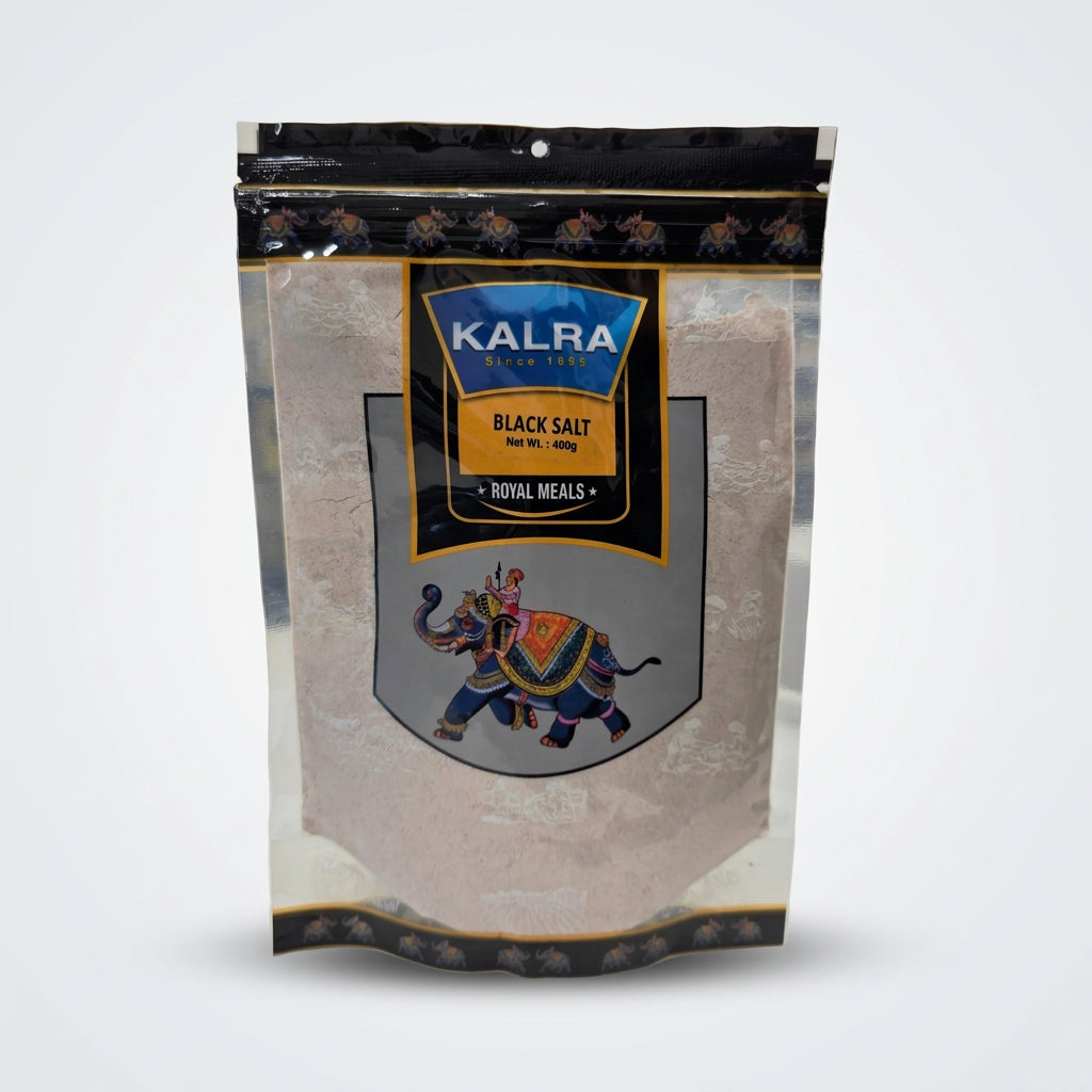 A stand-up pouch of Kalra Black Salt (Royal Meals) sitting on a white counter in a grocery store aisle. The packaging features a black top and bottom border, a blue and gold central logo, and an illustration of an elephant carrying a mace.