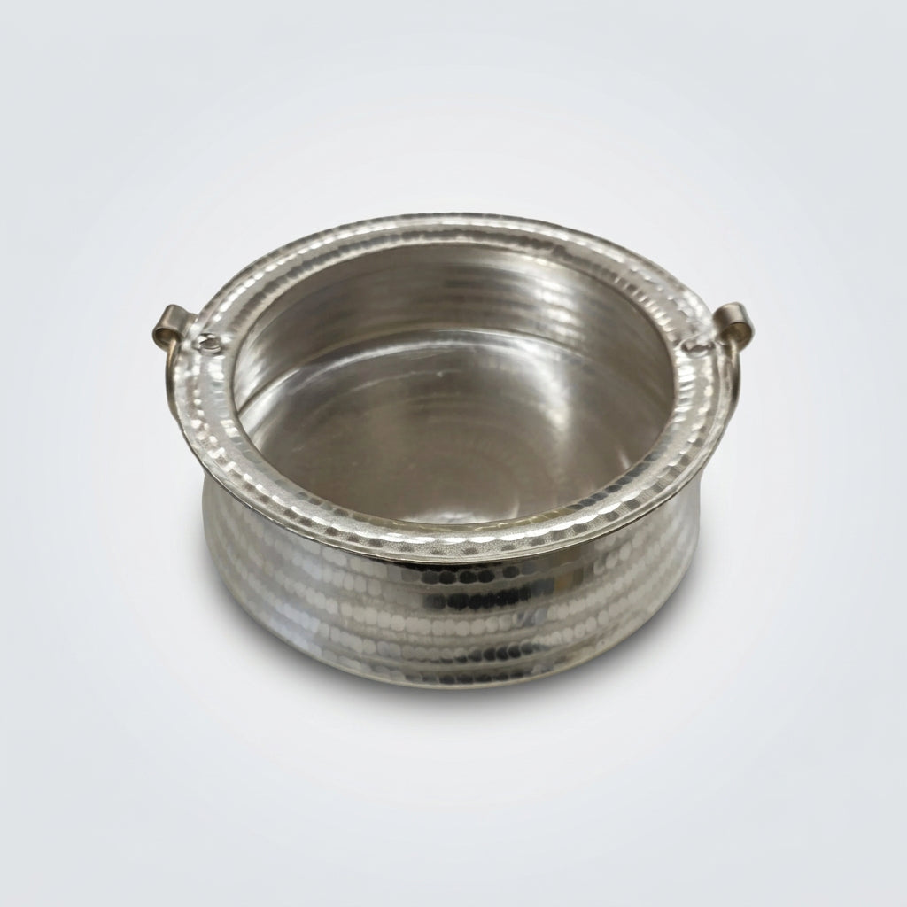 A small hammered silver-toned metal pot or container with two side handles, photographed on a white tabletop.