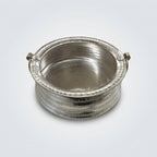 A small hammered silver-toned metal pot or container with two side handles, photographed on a white tabletop.