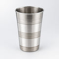 A silver-colored steel glass is placed on a white surface with a small potted plant beside it.