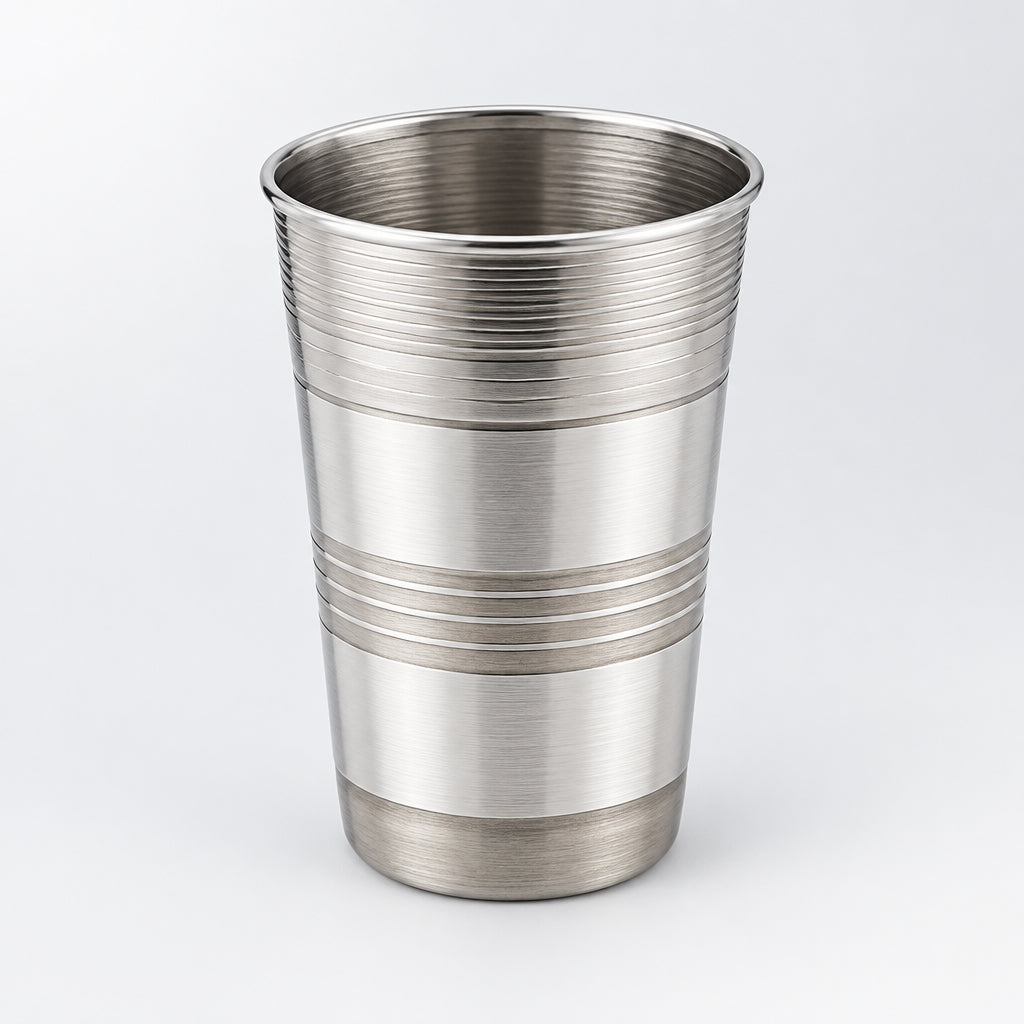 A silver-colored steel glass is placed on a white surface with a small potted plant beside it.