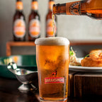 Beer being poured into a Bara Singhhe glass with bottles in the background.