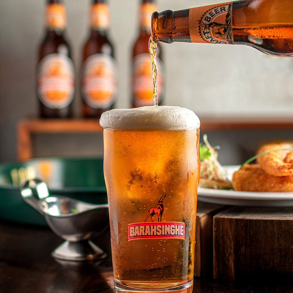 Beer being poured into a Bara Singhhe glass with bottles in the background.