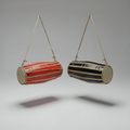 Two hanging cylindrical drums, one red and one black and gold, on a gray background.