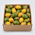 A cardboard box filled with small oval fruits that are mostly yellow with green patches, photographed from above on a light gray background.