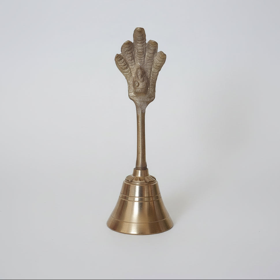A small bronze-colored metal bell with a hand-shaped figure on top.