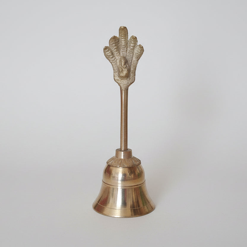 A brass bell with a design in the shape of a hand on the top, used for religious purposes.