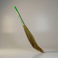 A traditional hand broom with a wooden handle and natural fiber bristles, predominantly green and brown in color.