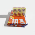 A set of dice with a design in yellow and red colors, placed on a table with a multicolored fabric featuring text and geometric patterns.