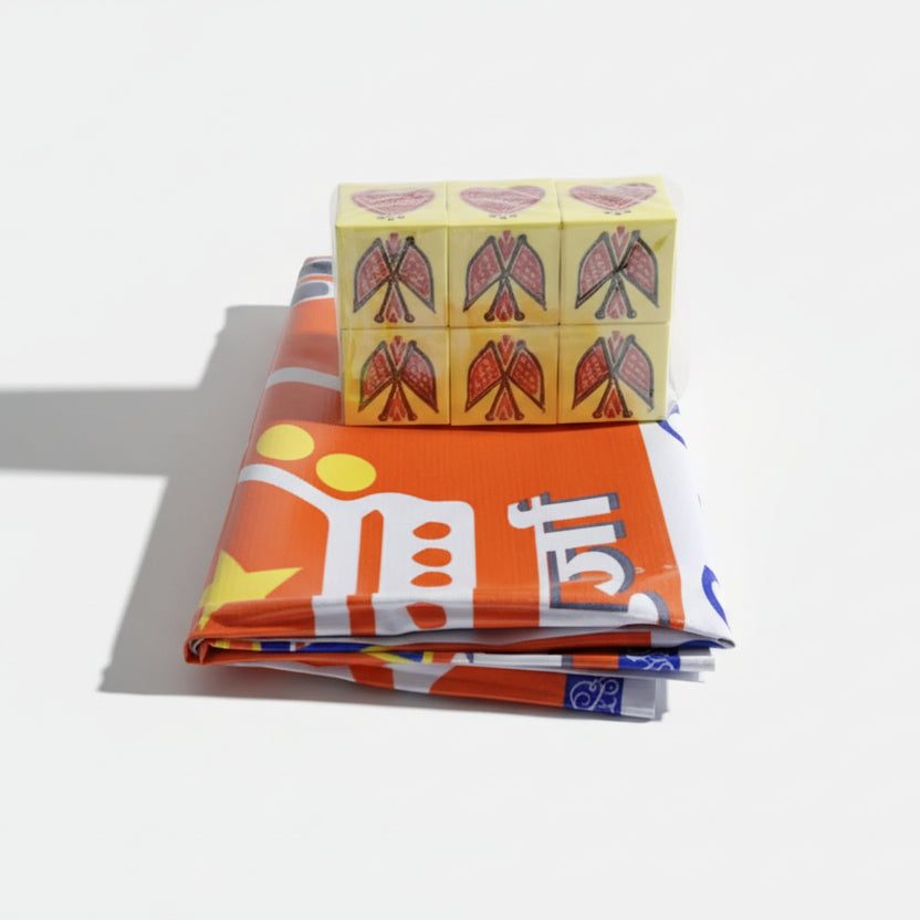 A set of dice with a design in yellow and red colors, placed on a table with a multicolored fabric featuring text and geometric patterns.